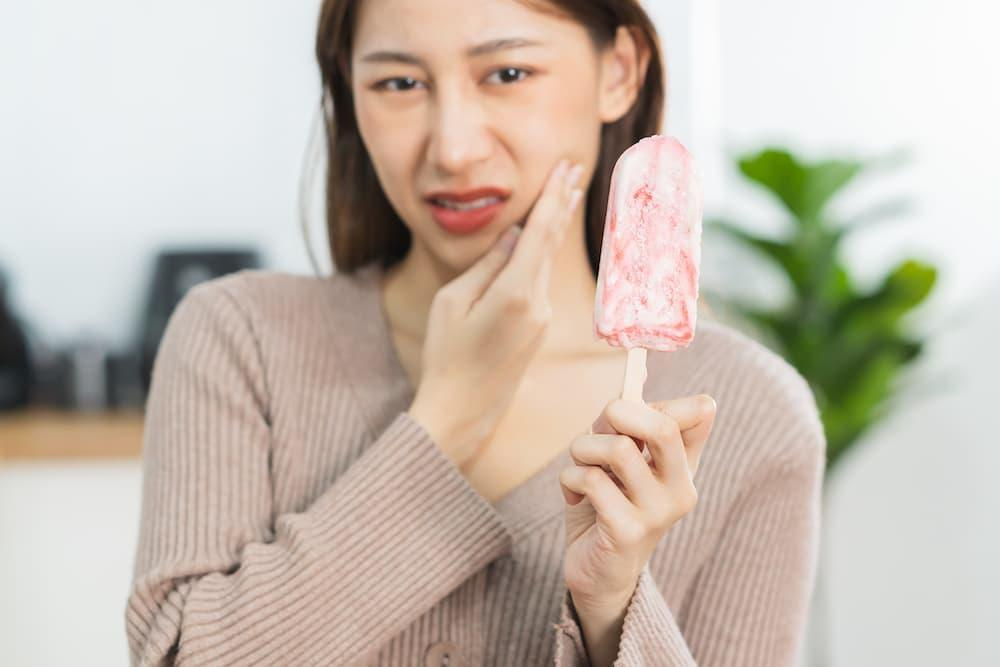 woman with a teeth pain and an ice cream in her hand